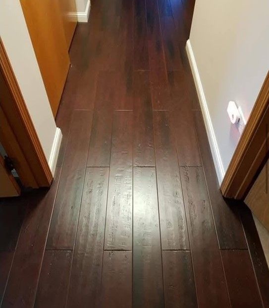 Dark wood flooring in a hallway with a door on each side, reflecting light.