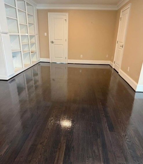 A room with polished dark wood floors, white built-in shelves, and two white doors against beige walls.