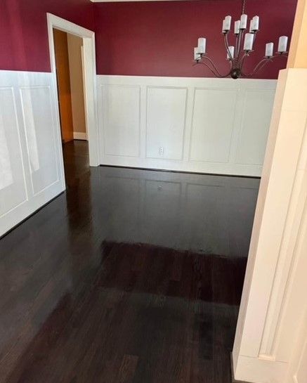 Dark hardwood floor in a room with white wainscoting and a red wall. A chandelier hangs from the ceiling.