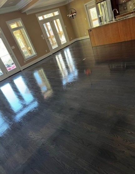 Dark stained hardwood floor reflecting light in a spacious room with windows and a kitchen island.