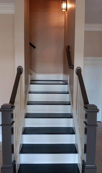 Staircase with black treads, white risers, and gray railings leads up. Light fixture is mounted on copper-colored wall.