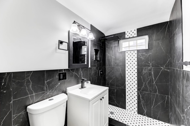A black and white photo of a bathroom with a toilet , sink , mirror and shower.