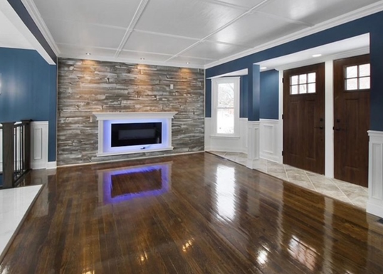 Living room with hardwood floor, blue walls, a rustic brick fireplace, and dark wooden double doors.