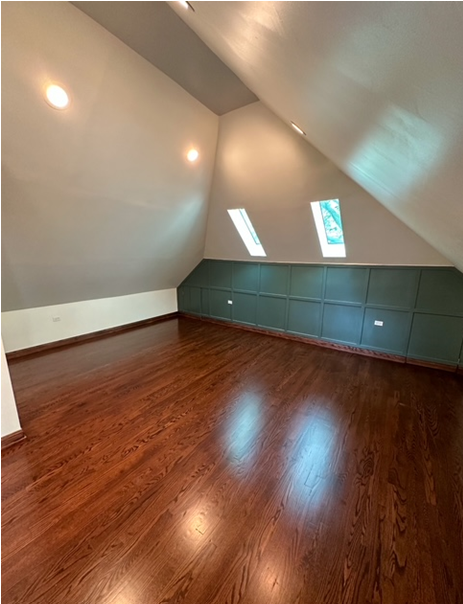 An empty attic with hardwood floors and a slanted ceiling.