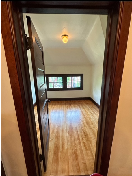 A doorway leading to an empty room with hardwood floors and two windows.