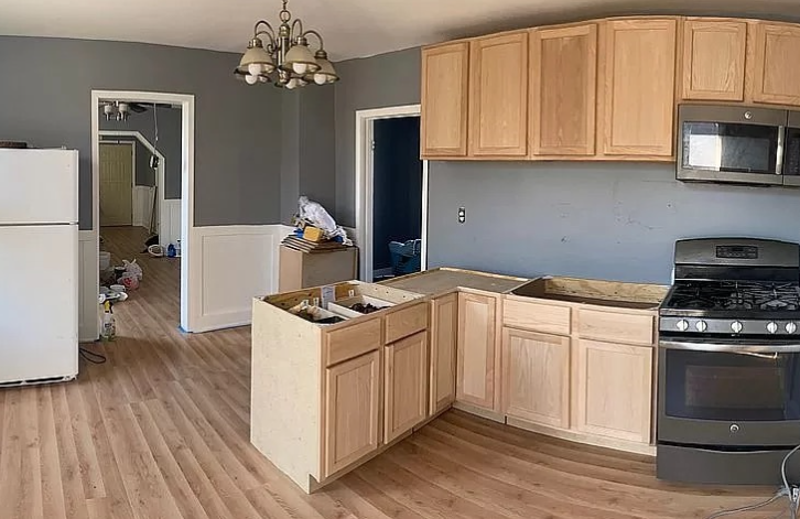 A kitchen with wooden cabinets , a stove , a refrigerator and a microwave.