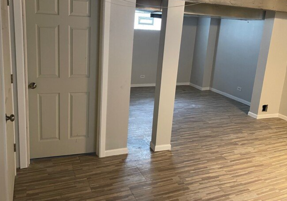 An empty basement with hardwood floors and a white door.