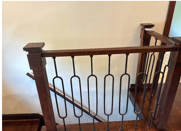 Wooden staircase railing with dark brown posts and railing, and black metal vertical accents.