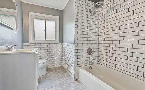 A bathroom with white brick walls , a tub , a toilet , and a window.