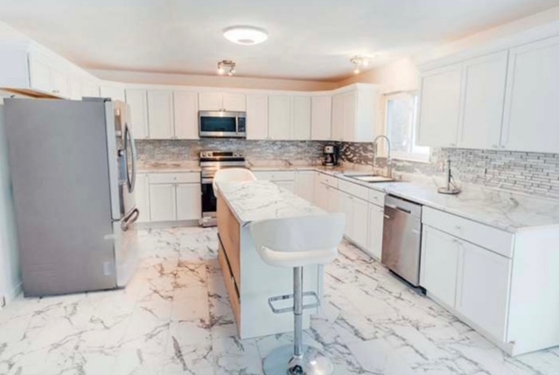 A kitchen with white cabinets , stainless steel appliances , and marble floors.
