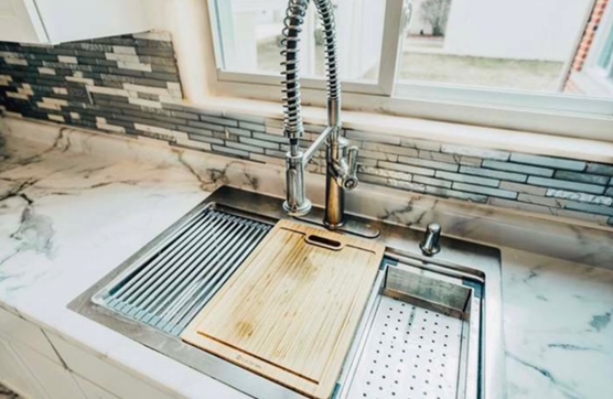 A kitchen sink with a wooden cutting board and a faucet.