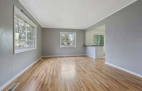 An empty living room with hardwood floors and gray walls.