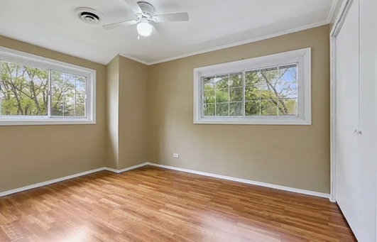 An empty bedroom with hardwood floors , two windows and a ceiling fan.