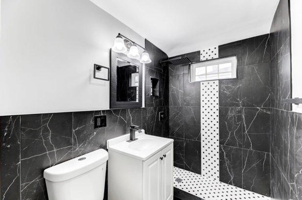 Bathroom with black marble tile, a white vanity, and a toilet. A small shower has a decorative white and black tile strip.