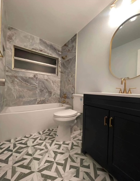 Bathroom with marble-look tile, dark blue vanity, gold fixtures, and patterned floor tile.