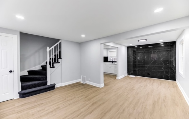 An empty basement with hardwood floors and stairs leading up to the second floor.