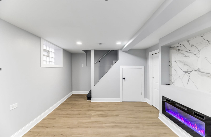 An empty basement with a fireplace and stairs.