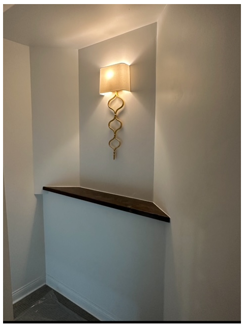 A built-in corner niche with a dark shelf, gold decorative sconce, and soft light against white walls.
