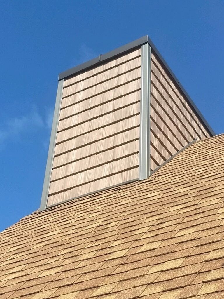 A wooden chimney on top of a roof with a blue sky in the background.