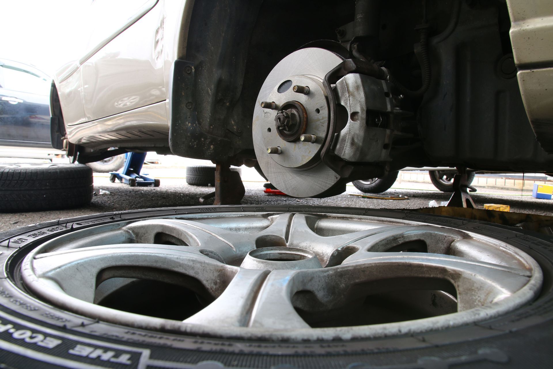Car with a tire removed, revealing brake assembly, with a tire on the ground in the foreground.