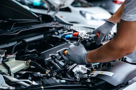 A man is working on the engine of a car with a wrench.