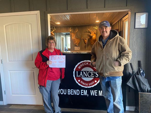Two people stand by a Lancaster sign inside a rustic room, one holding a sign.