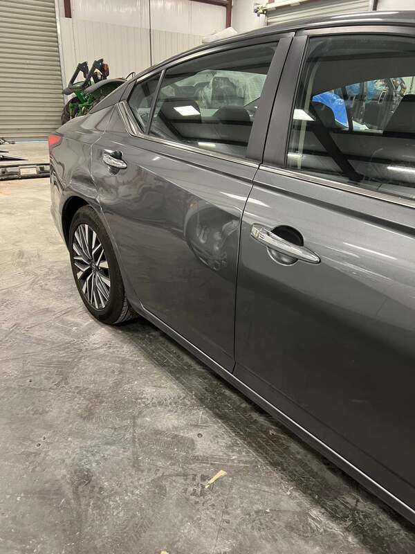 Gray sedan parked indoors with a damaged rear door and scuffed side panel