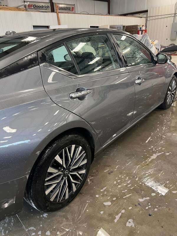 Gray sedan parked indoors in a garage, side view with wet floor and industrial background