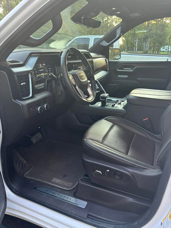 Black leather car interior with open driver door, steering wheel, center console, and front seat.