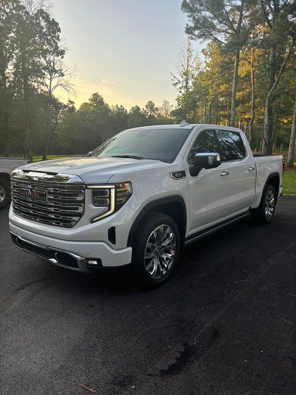 White GMC pickup truck parked on a tree-lined road at sunrise