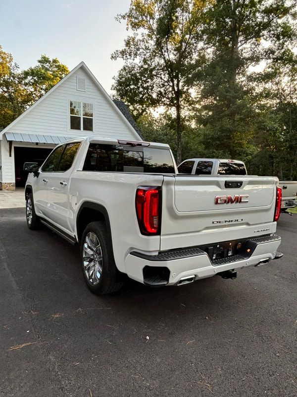 White GMC Sierra pickup parked in a driveway beside a white house at dusk