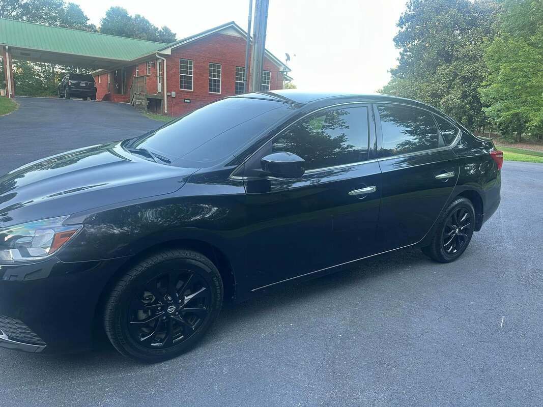 Black sedan parked on a driveway near a red house with a green-roofed carport.