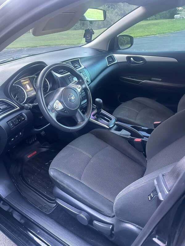 Car interior with black seats and steering wheel, seen from the open driver’s door.