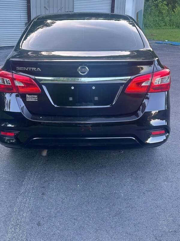 Black Nissan sedan parked on wet pavement, rear view with garage doors in the background.