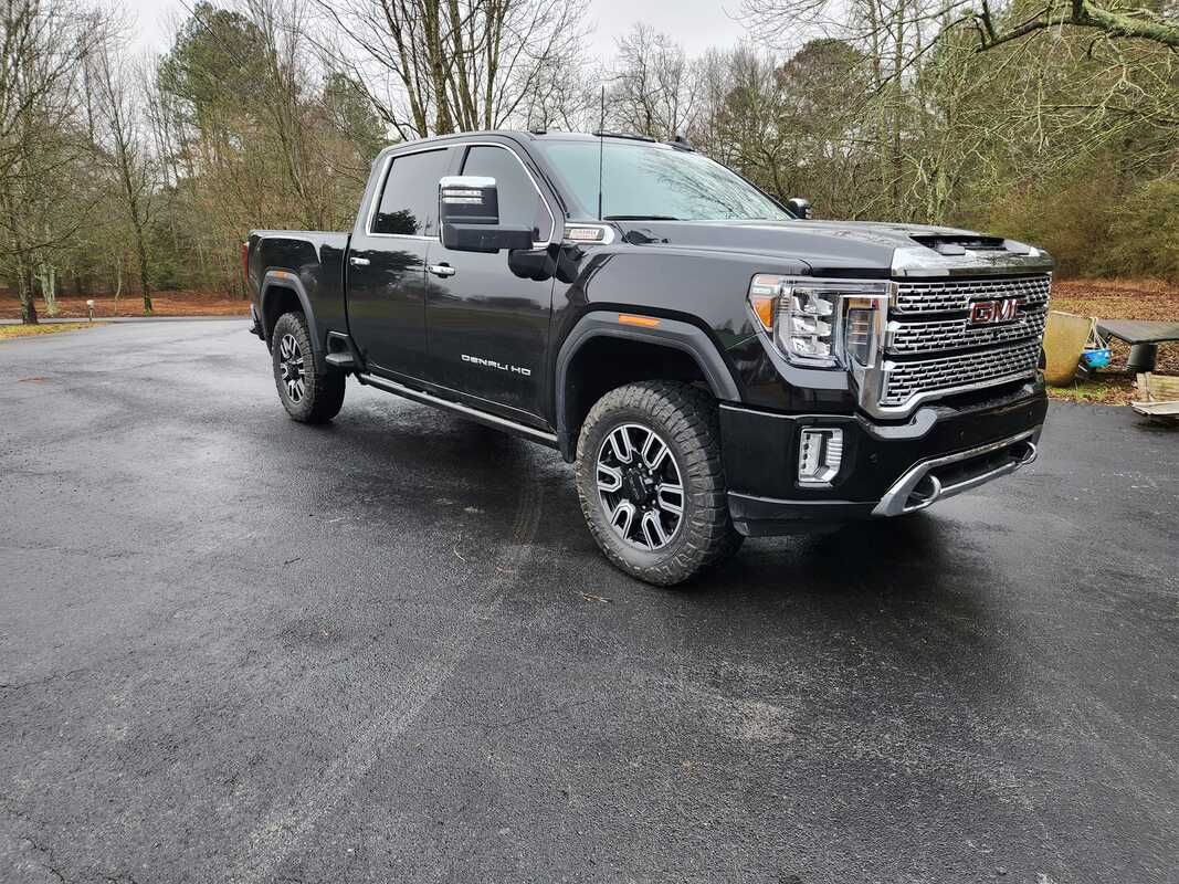 Black GMC pickup truck parked on wet pavement in a wooded lot