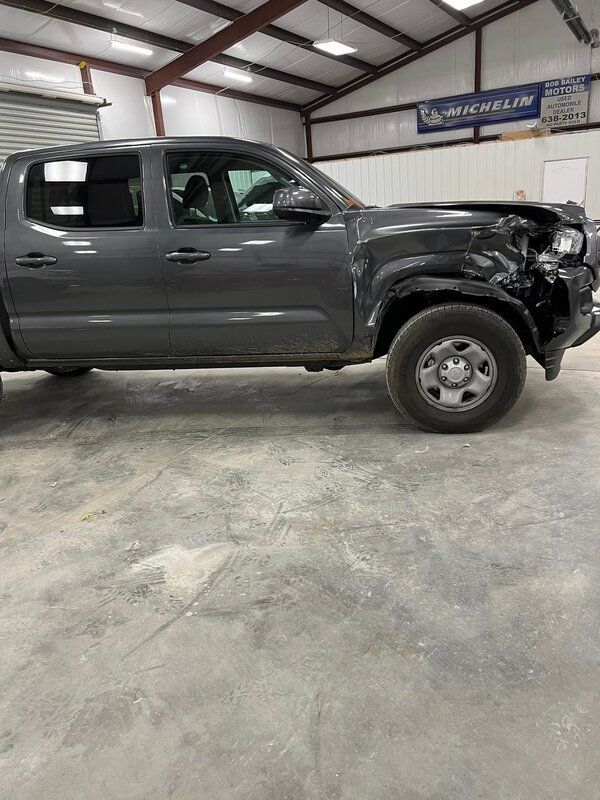 Gray pickup truck in a garage, with front-end damage and a missing bumper.