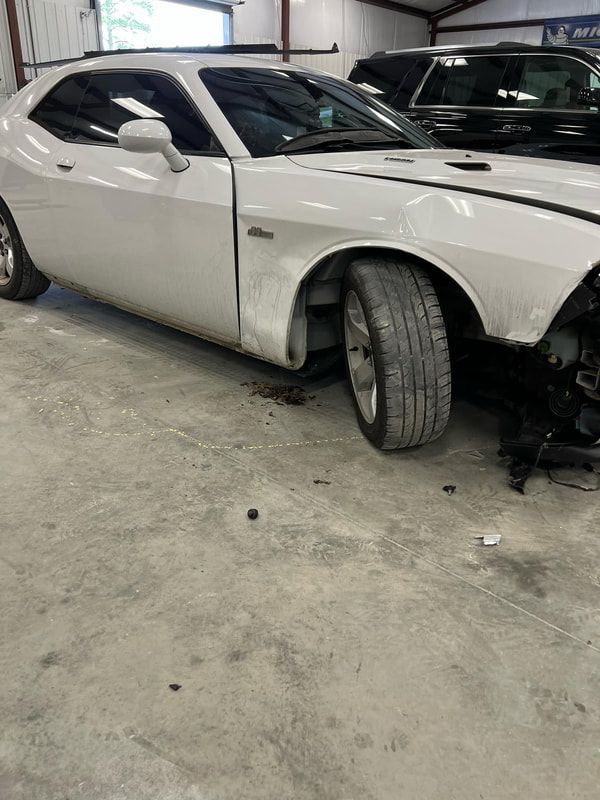 White sports car in a garage with the front end partially disassembled and the front wheel turned outward