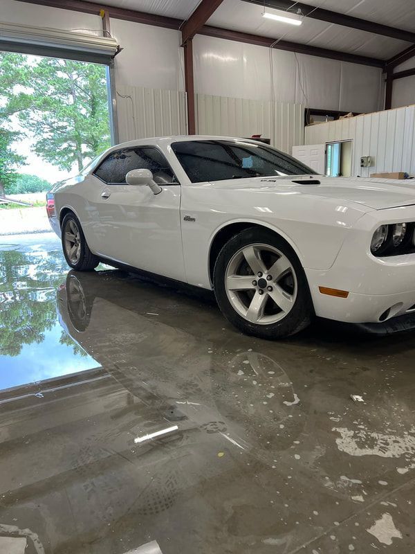 White Dodge Challenger parked inside a garage with a wet concrete floor.