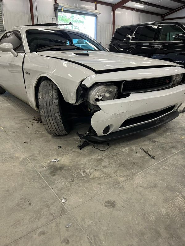 Damaged white sports car with front-end collision damage inside a garage