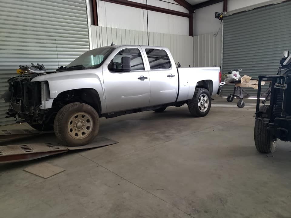 Silver pickup truck in a garage, missing front bumper, with a motorcycle nearby.