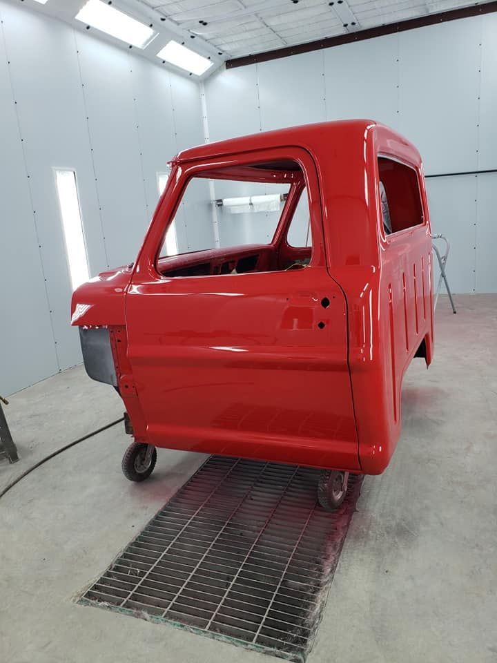 Red truck cab body in a paint booth, glossy red with no front grille or wheels