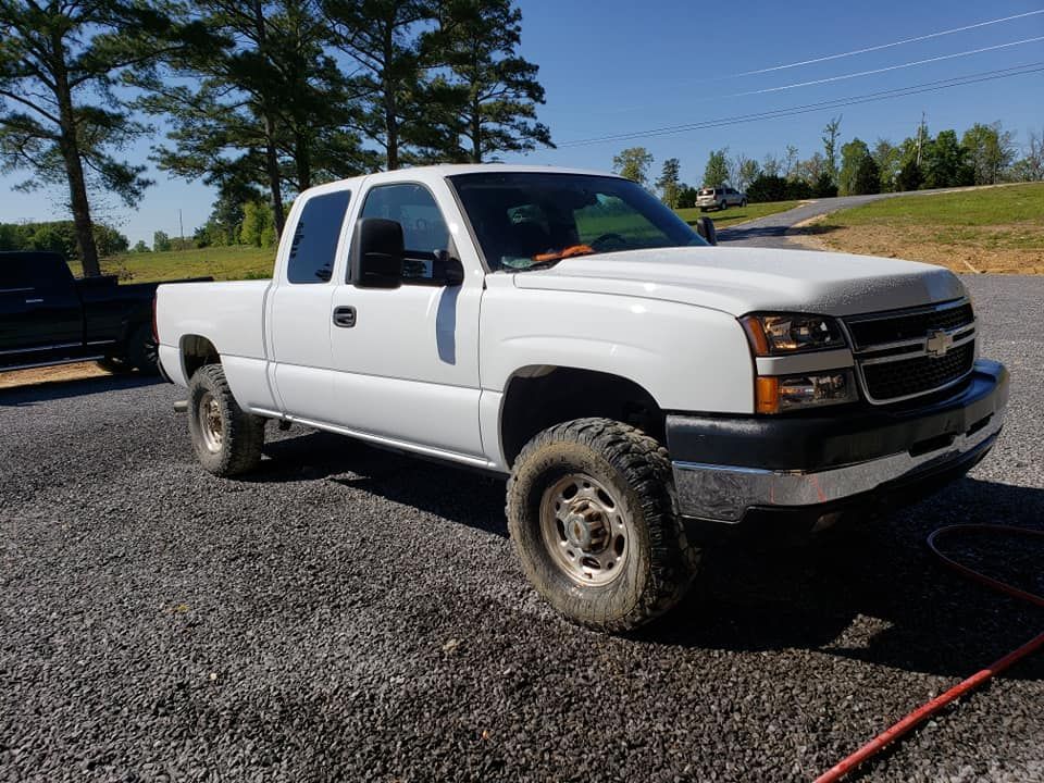 White lifted pickup truck parked on gravel in a sunny outdoor lot