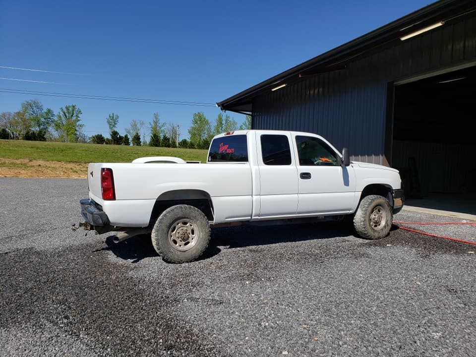 White pickup truck parked on gravel beside a dark barn on a sunny day