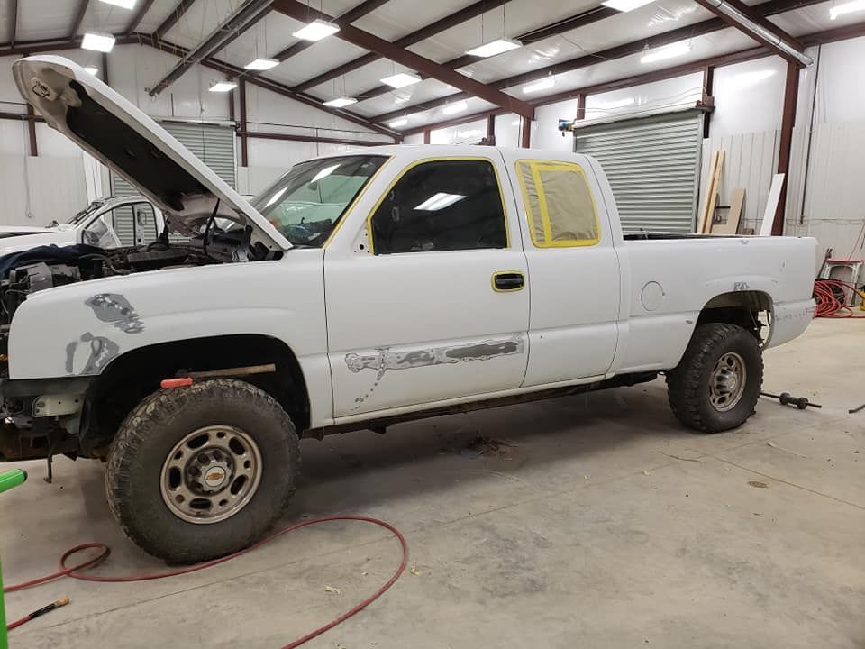 White pickup truck in a garage with hood open and bodywork underway