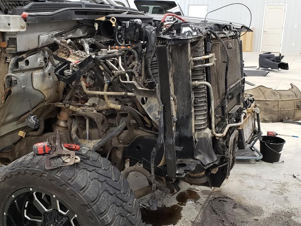 Damaged vehicle chassis with exposed engine and front tire in a garage, surrounded by tools and parts