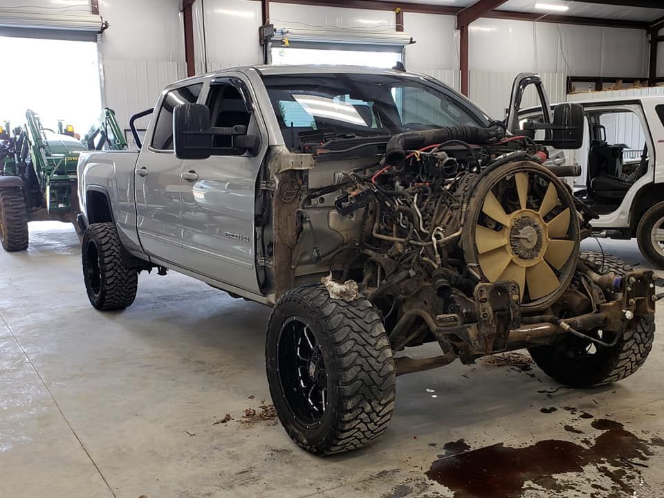 Damaged gray pickup truck in a garage, front end missing and exposed engine parts visible.