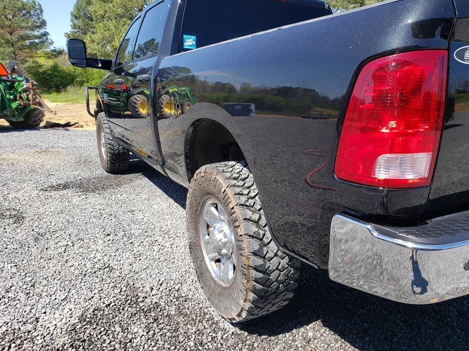 Black pickup truck with off-road tires parked on gravel in bright sunlight