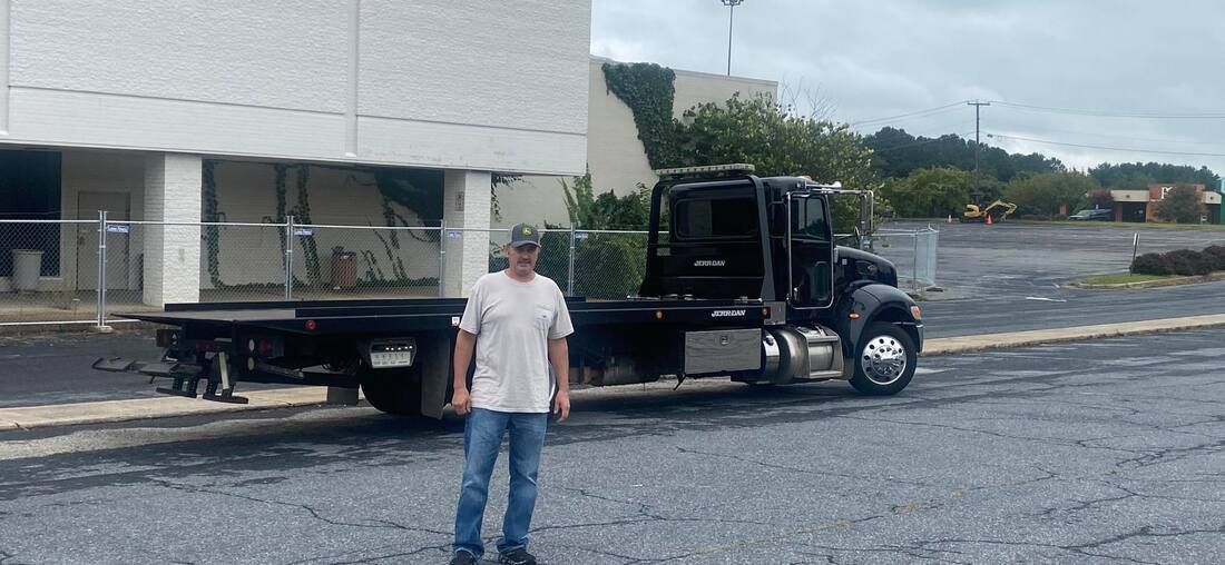 Man standing beside a black flatbed truck with a large white load in a parking lot
