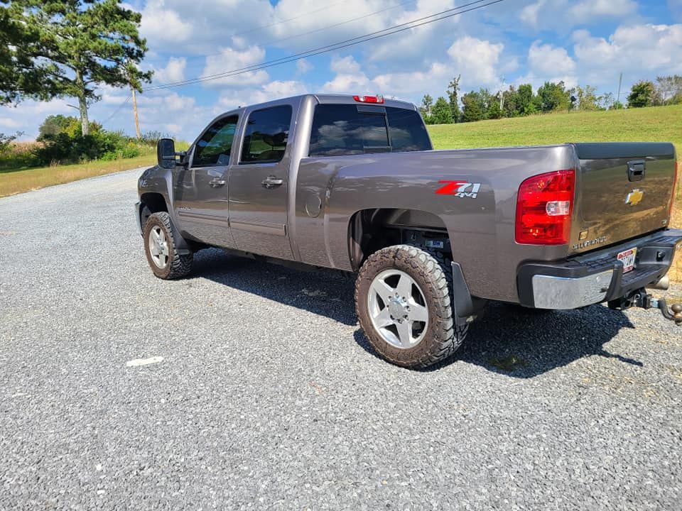 Gray pickup truck parked on a gravel road beside a grassy field under a blue sky.