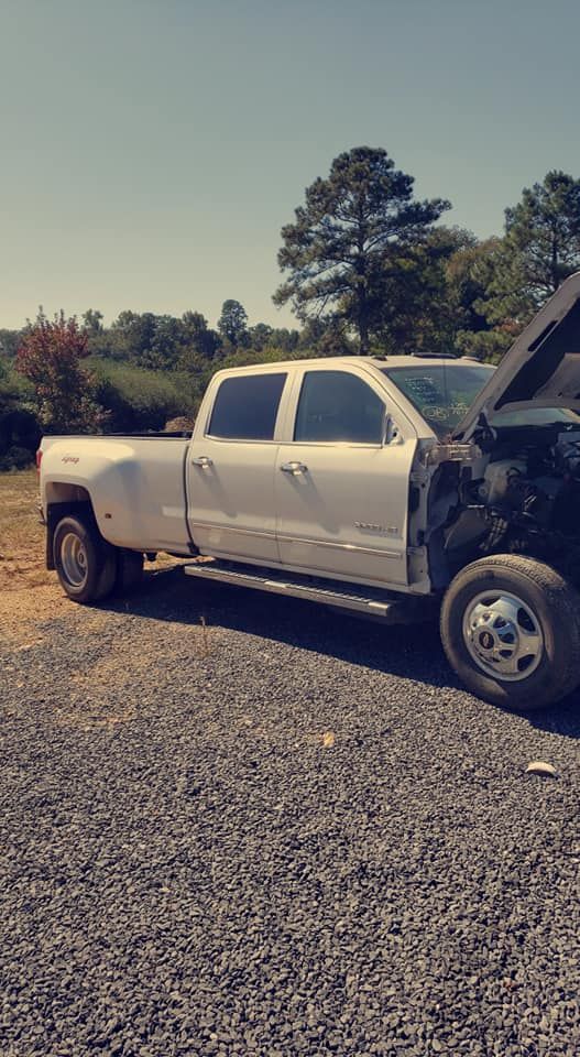 White pickup truck parked on gravel with hood open in a rural field